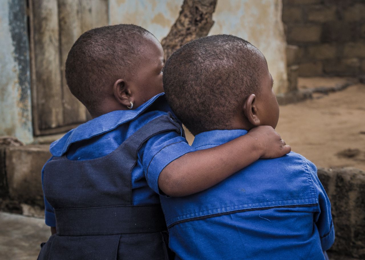 Two children in blue uniforms embrace, showing a heartwarming bond. Captured from behind.