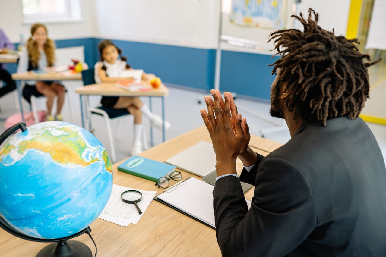 A teacher in a classroom with students, focusing on a globe for geography lesson.
